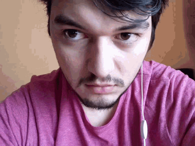 a man with a beard is wearing a pink shirt and headphones .
