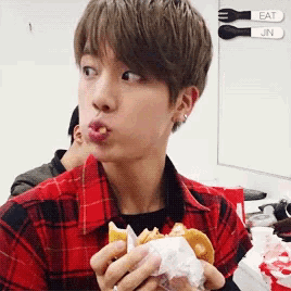 a man in a plaid shirt is eating a hamburger with a fork and knife behind him that say eat