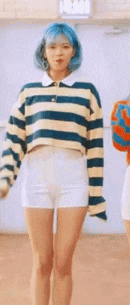 a woman with blue hair wearing a striped shirt and white shorts .