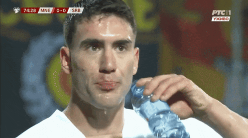 a man drinking water from a bottle while watching a soccer game
