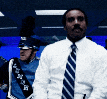 a man in a white shirt and blue tie is standing next to a man in a blue uniform with the word lun on it