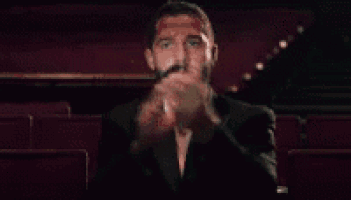 a man with a beard is sitting in a movie theater with his eyes closed and his hands on his chest .