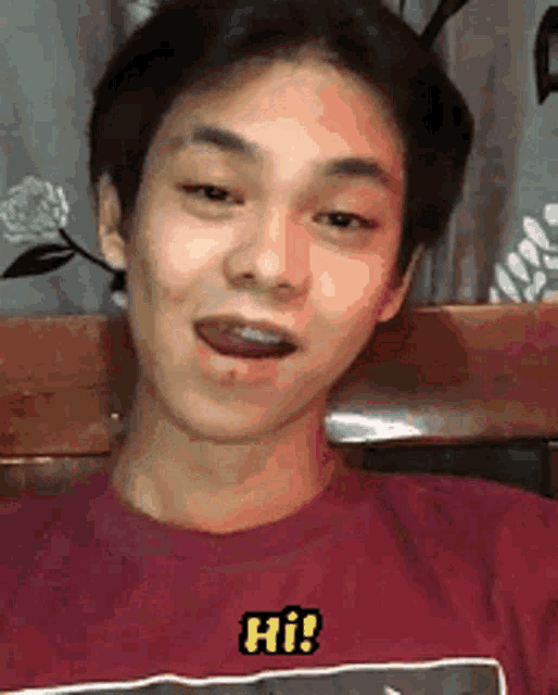 a young man wearing a red shirt with the word hi on it is sitting on a wooden bench .
