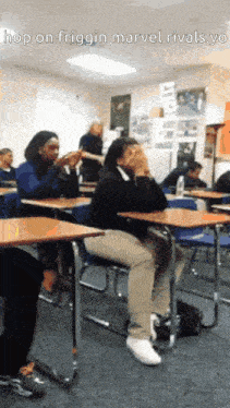 a group of people sit at desks in a classroom with the caption hop on friggin marvel rivals ye
