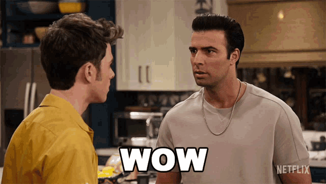 two men are standing in a kitchen and one has the word wow on his chest