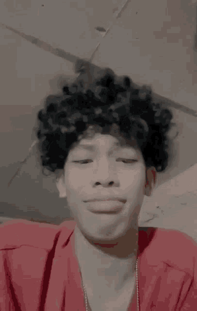 a young man with curly hair is making a funny face while wearing a red shirt .