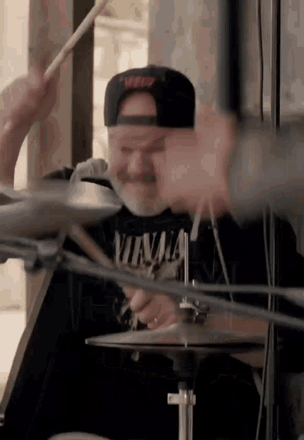 a man in a nirvana shirt plays drums