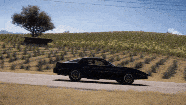 a black car is driving down a road near a field