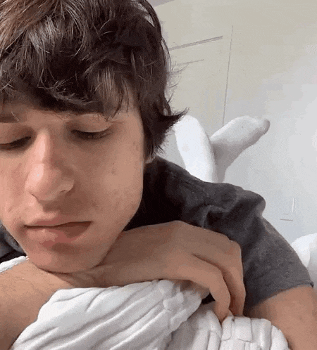 a young man is laying on a bed with his head on his arm and his eyes closed .