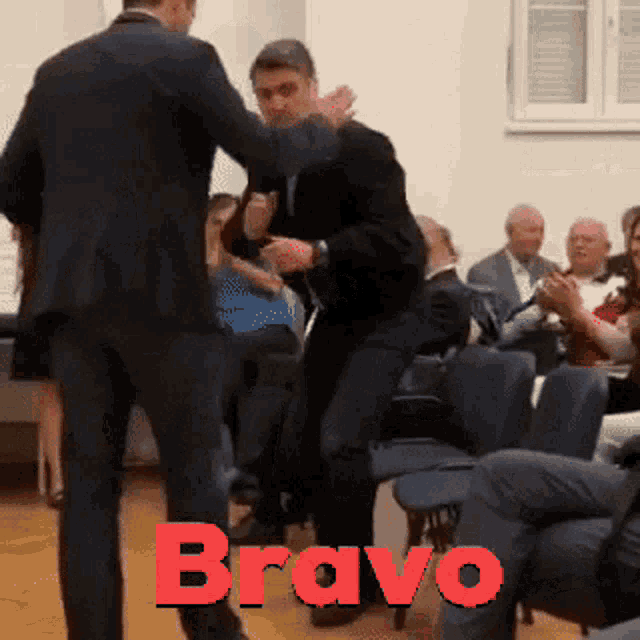 a man in a suit is dancing in front of a crowd with the word bravo on the bottom right