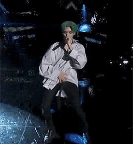 a man with green hair is singing into a microphone while standing on a stage .
