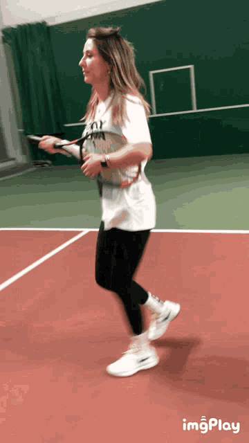 a woman holding a tennis racquet on a tennis court with imgplay written on the bottom right
