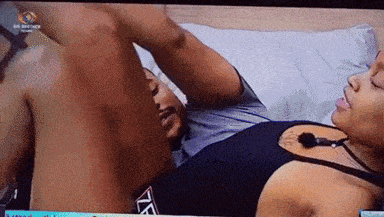 a man and a woman are laying on a bed and the man is wearing a black tank top with the letter t on the front