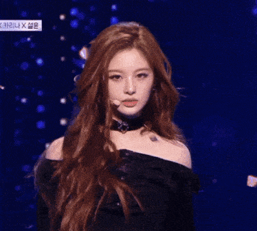 a woman with long red hair stands in front of a microphone in front of a blue background