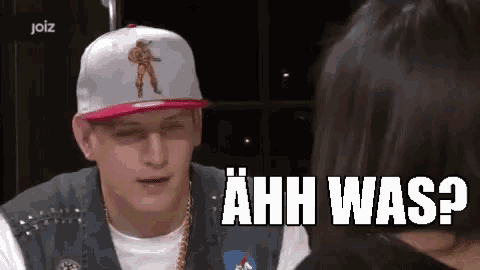 a man wearing a hat and a vest is talking to a woman and says ahh was