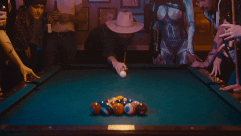 a man in a cowboy hat is playing pool in a dark room