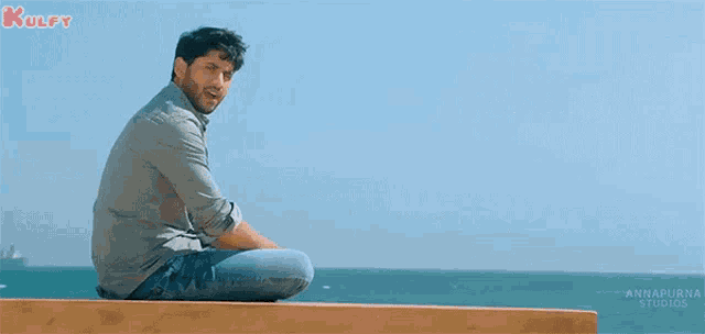 a man is sitting on a wooden ledge with the words kulfy in the upper left corner