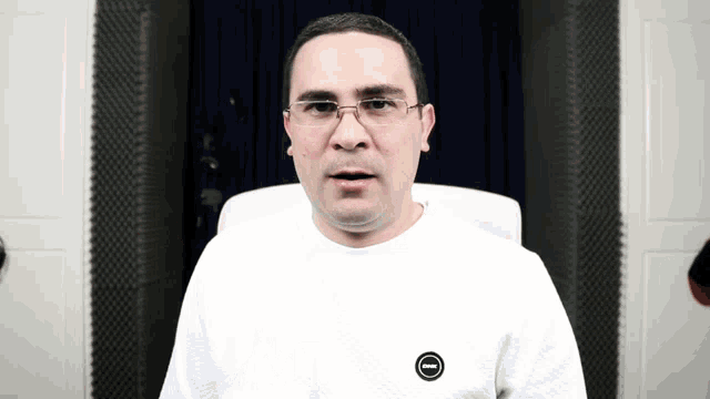 a man wearing glasses and a white shirt with a black circle on the sleeve