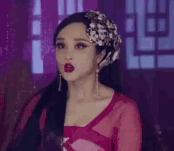 a woman with long black hair and red lips is wearing a pink dress and earrings .