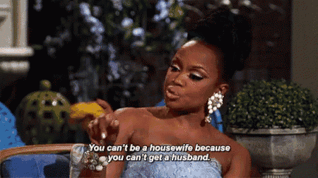 a woman in a blue dress is sitting in a chair and talking about being a housewife and getting a husband .