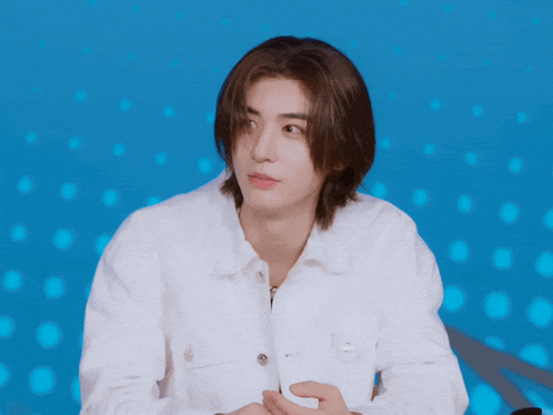 a young man with long hair and a white shirt looks at the camera