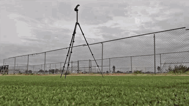 a camera on a tripod in a field with a chain link fence behind it