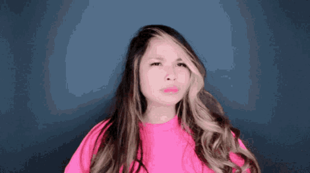 a woman with long hair and a pink shirt is making a funny face