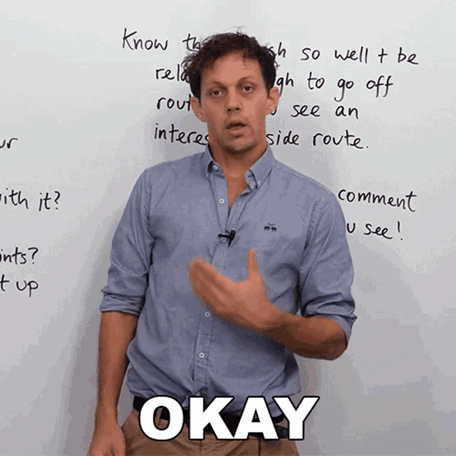 a man in a blue shirt stands in front of a whiteboard that says okay