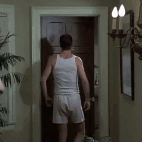 a man in a white tank top is standing in a doorway smoking a cigarette
