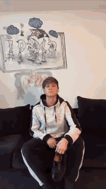 a boy sits on a couch in front of a drawing of a cow on the wall