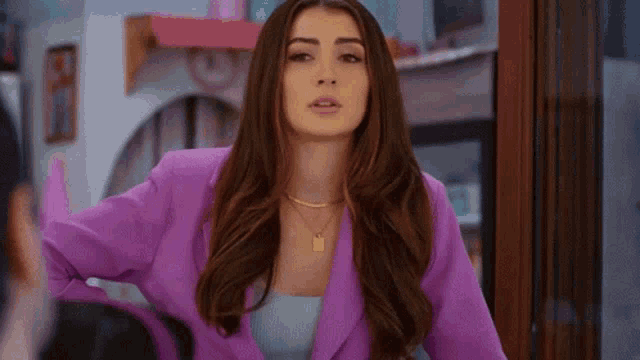 a woman in a purple jacket is standing in front of a window .