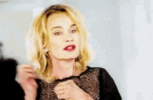 a woman with blonde hair and red lipstick is wearing a black top and a ring .
