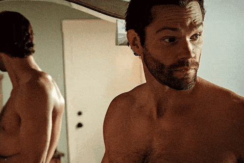 a shirtless man is looking at himself in a mirror .