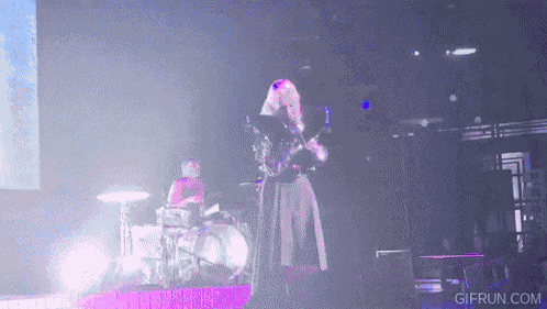 a woman is playing a guitar on a stage while a man plays drums .