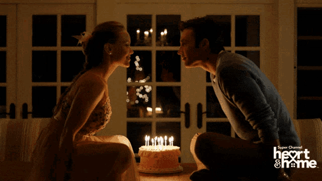 a man and a woman kissing in front of a birthday cake with candles