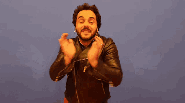 a man wearing a black leather jacket with his arms outstretched against a blue background