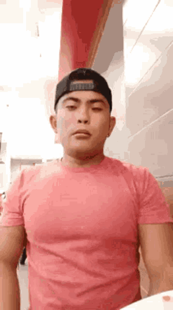 a man wearing a pink shirt and a black hat is making a face .