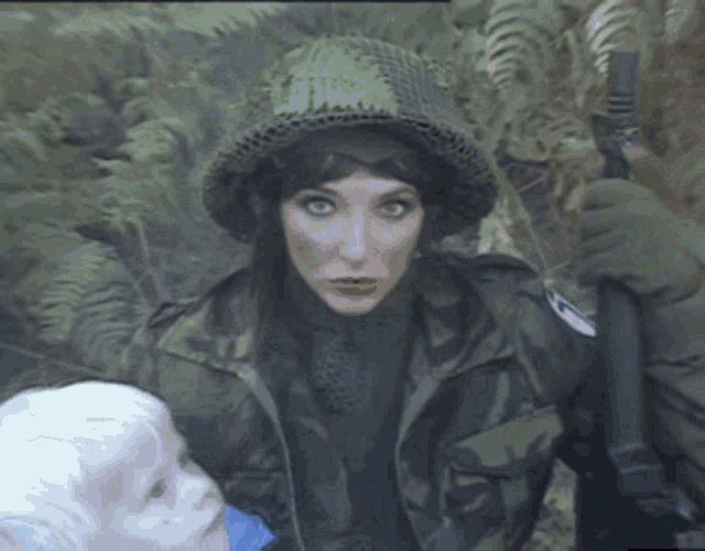 a woman in a military uniform is holding a gun and looking at a little boy