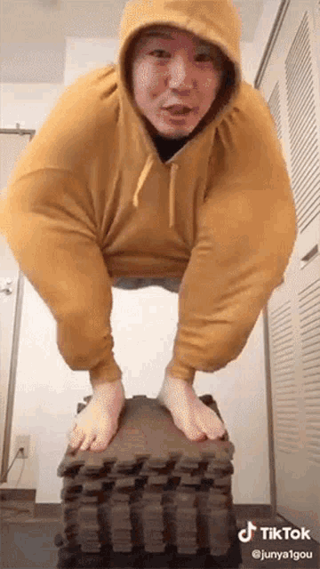 a man in a yellow hoodie is balancing on a stack of foam mats