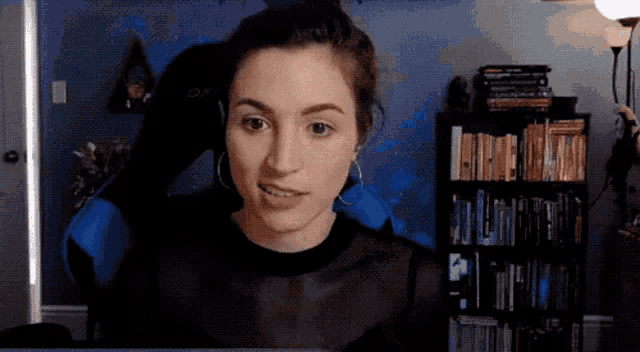 a woman is sitting in front of a bookshelf wearing earrings