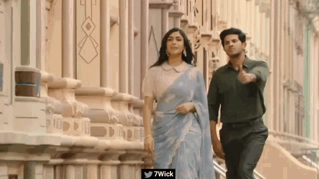 a man and a woman are walking in front of a building with 7wick written on the bottom of the image