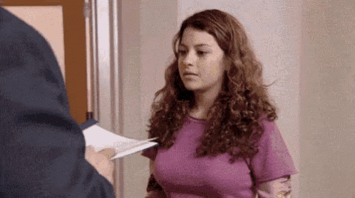 a woman in a purple shirt is standing in front of a door while a man holds a piece of paper .