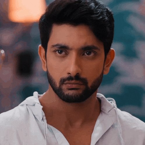 a man with a beard wearing a white shirt looks at the camera