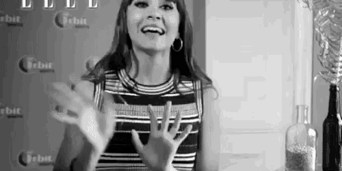 a black and white photo of a woman in a striped dress making a peace sign with her hands .