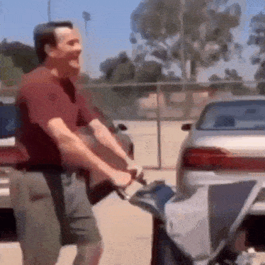 a man in a red shirt is pushing a stroller in a parking lot .