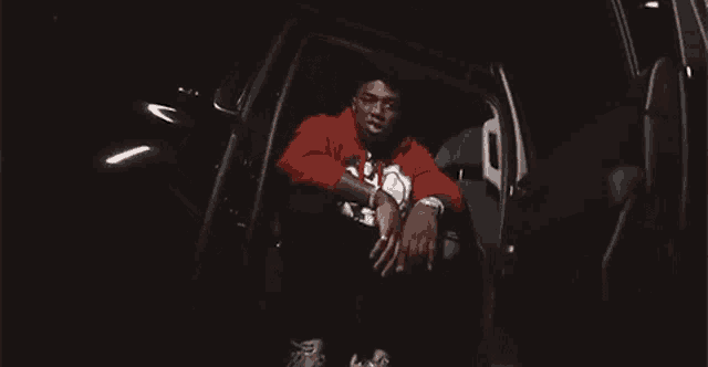a man in a red shirt is laying upside down in the back seat of a car .