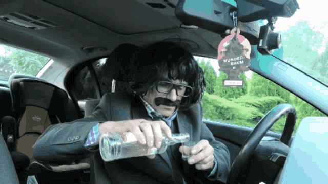 a man in a car with a wunder baum air freshener hanging from the rear view mirror
