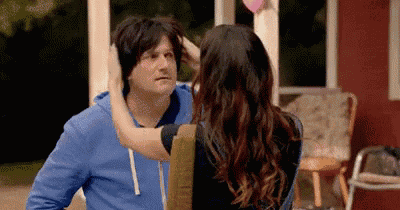 a woman is touching a man 's head while standing next to him .