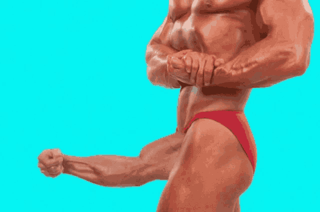 a bodybuilder in red shorts is flexing his muscles on a blue background .
