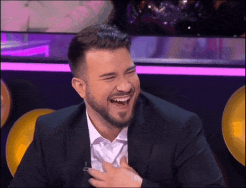 a man in a suit and white shirt is laughing with his hands on his chest